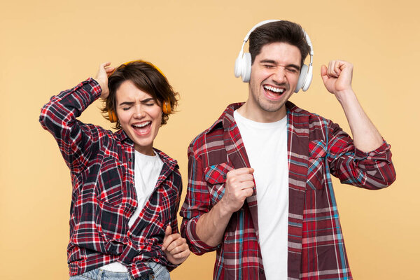 Portrait photo of cheerful, happy people, listening to music with stylish headphones, actively dancing, isolated on a yellow backdrop, eyes closed