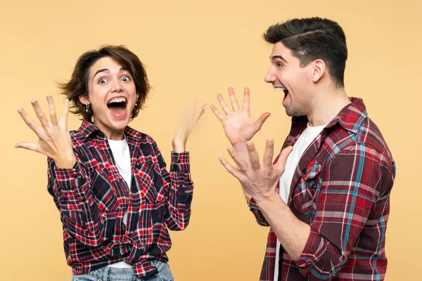 Portrait photo of an overjoyed people, excited woman and a surprised man, gesticulating as winners, celebrating an unbelievable victory, posing on a yellow background and looking at the camera