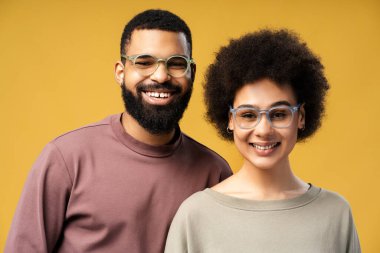 Gülümseyen, mutlu Afro-Amerikan kadın gözlüklü adam ve kadının portresi, sarı arka planda izole bir şekilde duran kameraya bakıyor. Görüş, tedavi, sağlık hizmetleri kavramı