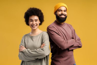 Neşeli, gülümseyen Afro-Amerikan çift, şık sarı şapkalı adam, kıvırcık saçlı mutlu kadın, sarı arka planda tek başına duran çapraz kollu kadın. İlişki kavramı