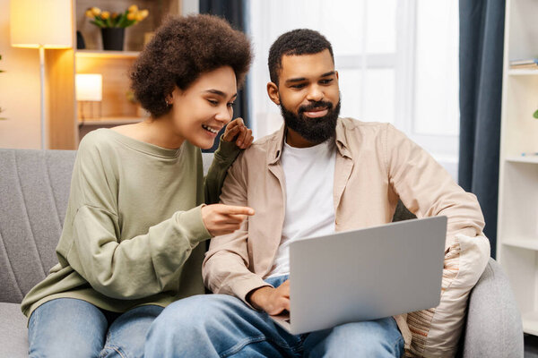 Portrait of busy smiling African American man and woman, freelancers using laptop, planning project, startup, working at home, sitting on comfortable sofa. Concept of remote job, online technology