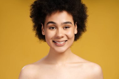 Çekici, seksi, şehvetli Afrikalı Amerikalı genç bir kadın kameraya bakıp gülümsüyor. Sarı arka planda izole edilmiş güzel bir kadın model. Reklam konsepti, doğal güzellik.