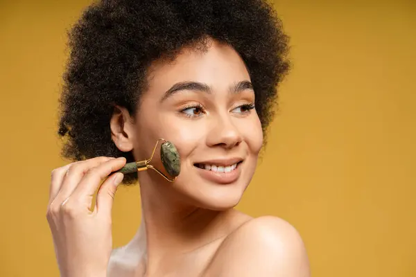 Atraktivní Šťastná Afroameričanka Kudrnatými Vlasy Která Masíruje Obličej Masážním Válečkem — Stock fotografie