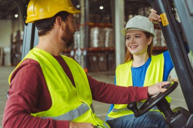 Sıkı şapkalar takan ve iş kıyafetleri giyen pozitif işçiler birbirleriyle iletişim kuruyor, adam forklift kullanıyor, depoda çalışıyor. Ulaşım, işbirliği, iletişim kavramı