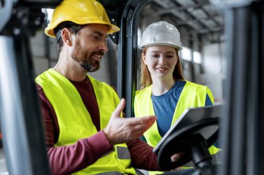 Kask takan ve birbirleriyle iletişim kuran yakışıklı meslektaşlar, forklift kullanan adam, dijital tablet kullanan, depoda çalışan mobil uygulama. Ulaşım, işbirliği, iletişim kavramı