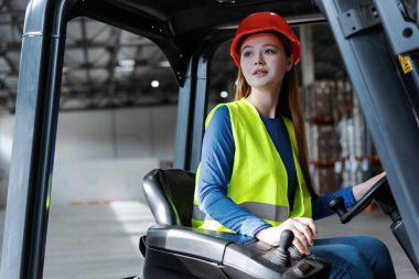 Güzel, sevimli bayan işçi, sıkı şapka takan ve forklift kullanan, başka tarafa bakan genç bir kadın. Çekici mühendis sürücü deposu. Lojistik, ulaşım, araç kavramı