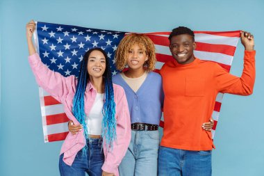 Heyecanlı Afrikalı Amerikalı arkadaşlar ellerinde Amerikan bayrağı, kameraya bakıyorlar, mavi arka planda izole olmuşlar. Seçim sonuçları konsepti bekleniyor 