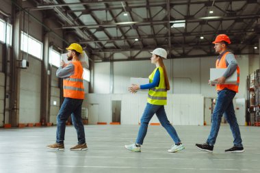 Profesyonel yükleyicilerden oluşan bir grup, kutuları depoya taşıyor. Güvenlik kaskı ve iş kıyafetleri takan genç erkekler ve kadınlar. Lojistik, dağıtım, dağıtım kavramı