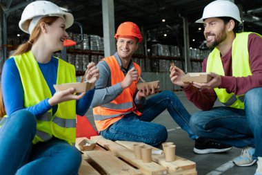 Bir grup güler yüzlü işçi sert şapka, yelek giyer, beslenme çantalarını tutar, yemek yer, oturur ve teneffüste birbirleriyle konuşurlar. Öğle yemeği kavramı.