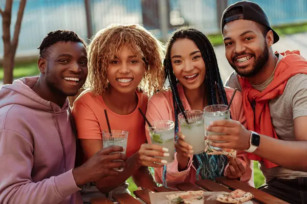 Group of diverse smiling African American friends, meeting at birthday party, sitting in cafe, drinking lemonade and looking at camera outdoors. Celebration concept