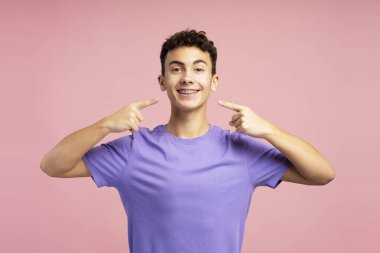 Genç, diş telleriyle dişlerini gösteren genç bir çocuk pembe arka planda izole bir şekilde duran kameraya bakıyor. Bakım ayrıntıları, sağlık hizmetleri kavramı