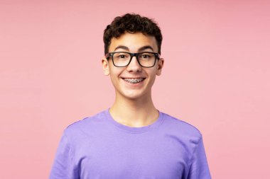 Gülümseyen mutlu çocuk portresi, gözlüklü genç sarı arka planda izole bir şekilde kameraya bakıyor. Görüş, tedavi, sağlık hizmetleri kavramı