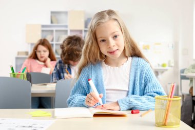 Sınıfta sınıf arkadaşları arka planda çalışırken gülümseyen liseli kız. Eğitim konsepti. Okula geri dön.