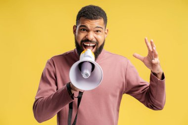 Sakallı Afrikalı Amerikalı adam stüdyoda poz verirken megafona bağırıyor ve sarı arka planda izole edilmiş kameraya bakıyor. Halk yaşam tarzı konsepti