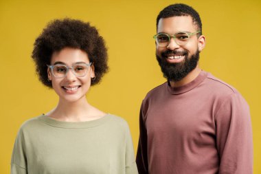 Stüdyoda sarı arka planda izole edilmiş kameraya bakarken şık gözlükler takan Afro-Amerikan kadın ve erkekler. Yaşam tarzı insan konsepti