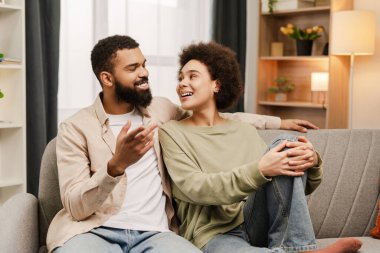 Gülümseyen Afro-Amerikan erkek ve kadın evdeki kanepede oturup sarılırken, hafta sonunun tadını çıkarırken. İlişki, flört kavramı