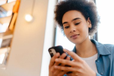 Otantik, çekici Afro-Amerikan kadın elinde cep telefonu, kısa mesaj, çevrimiçi alışveriş, fotokopi alanı. Çevrimiçi teknoloji kavramı