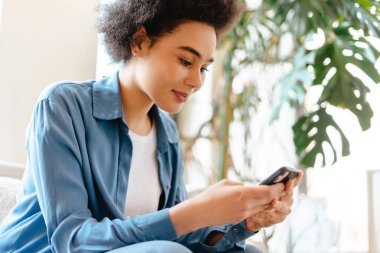 Gülümseyen, güzel Afro-Amerikan genç bir kadın elinde cep telefonu, kısa mesaj, çevrimiçi alışveriş, fotokopi alanı. Çevrimiçi teknoloji kavramı, sosyal medya