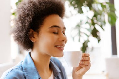 Kapalı gözlü, neşeli Afro-Amerikan kadının yakından çekilmiş portresi. İçkinin ve kahvenin tadını çıkarıyor. Sabah rutini, kahvaltı kavramı