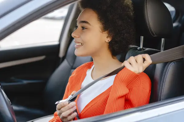 美しく 笑顔で 若いアフリカ系アメリカ人女性 カーリーヘアのドライバーは カーサロンに座ってシートベルトを締める 自動車保険について ロイヤリティフリーのストック画像
