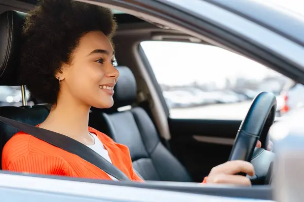 ハッピー笑顔の魅力的なアフリカ系アメリカ人女性 カーリーヘア運転車 バックルセーフティベルト 輸送コンセプト ストック画像