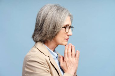 Senior sad businesswoman in eyeglasses looking away and thinking problems isolated on blue background. Stress, depression concept clipart