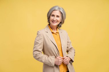 Smiling senior business woman, manager, financier looking at camera isolated on yellow background. Portrait of confident gray haired politician. Successful business, career clipart