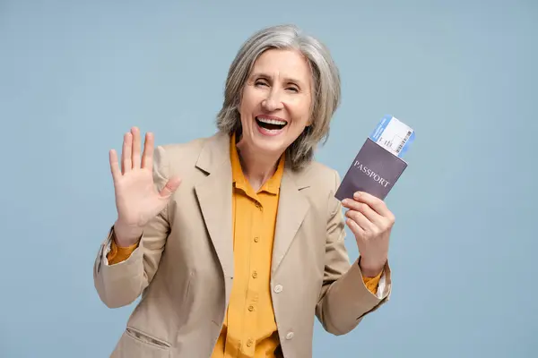 青い背景にパスポートとチケットを持っているハッピーポジティブグレーハイレッドシニア女性は 搭乗券を保持し 今後のフライトを楽しんでいます 海外旅行で引退した旅行者 ロイヤリティフリーのストック写真