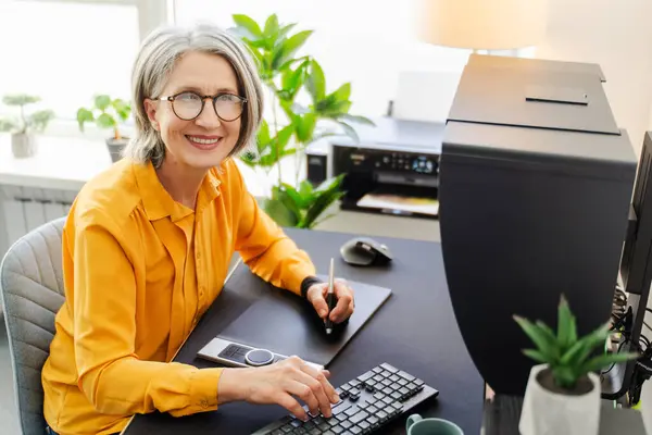 現代のオフィスで働く職場でタブレットを使用して シニア女性 グラフィックデザイナー 編集者を微笑む肖像画 テクノロジー 成功したビジネスコンセプト ストック写真