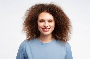 Çekici, kıvırcık saçlı, şık, mavi tişörtlü, beyaz arka planda yalnız poz veren genç bir kadın. Reklam kavramı, alışveriş.