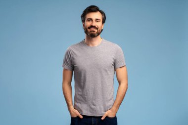 Stüdyoda poz veren, mavi arka planda izole edilmiş, pozitif sakallı genç adamın portresi. Reklam kavramı