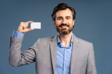 Mavi arka planda izole edilmiş, stüdyoda poz veren, boş kartvizitli genç bir işadamının portresi. Başarı, kariyer, iş konsepti