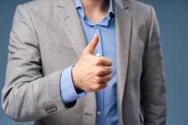 Takım elbiseli işadamının eli havada, stüdyoda poz veriyor, mavi arka planda izole. Başarı, kariyer, iş konsepti