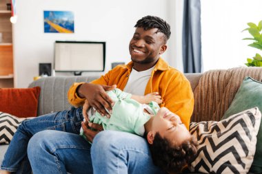 Yakışıklı, gülümseyen Afrikalı Amerikalı bir adam, genç bir baba oğluyla oynaşıyor, onu gıdıklıyor, evdeki rahat odada birlikte kanepede oturuyor. Ebeveynlik kavramı, çocukluk