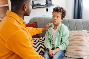 Rahat bir odada rahat bir kanepede otururken küçük bir oğluyla konuşan Afrikalı Amerikalı bir adamın portresi. İlişki konsepti, ebeveynlik, iletişim