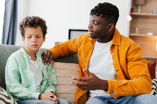 Çekici, Afro-Amerikan bir adam rahat bir odada rahat bir kanepede otururken küçük, gücenmiş oğlunu teselli ediyor. İlişki konsepti, ebeveynlik