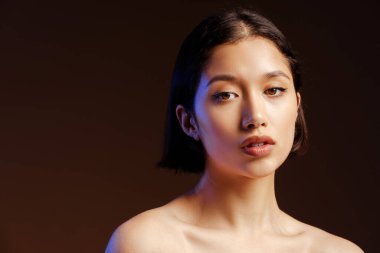 Koyu renk saçlı genç bir kadının güzel portresi. Taze parlayan sağlıklı cildiyle kameraya bakıyor, izole edilmiş siyah arka planda çıplak poz veriyor.