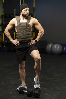 Attractive, serious Caucasian athlete, muscular man wearing weight plate, doing sports, training in gym, looking away. Healthy lifestyle concept
