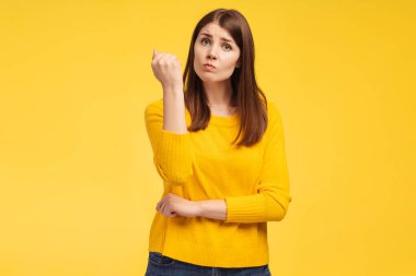 Kızgın, üzgün, orta yaşlı bir kadın, tehdit edici hareketler yapıyor, kameraya bakıyor ve sarı arka planda tek başına duran yumruğunu gösteriyor. Olumsuz duygular kavramı