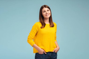 Gülümseyen, beyaz, orta yaşlı, şık kıyafetler giyen, elleri ceplerinde mavi arka planda izole bir şekilde kameraya bakan güzel bir kadının portresi. Reklam kavramı, alışveriş.