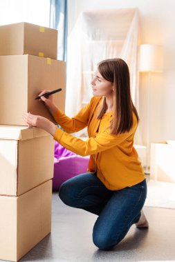 Güzel, neşeli kadın paketçi, karton kutuları paketliyor, imzalıyor, dairede, yeni eve taşınıyor. Kriz kiralama kavramı