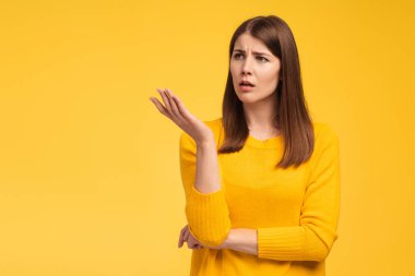 Serious sad middle aged woman looking away on copy space, misunderstanding standing isolated on yellow background. Advertisement concept clipart