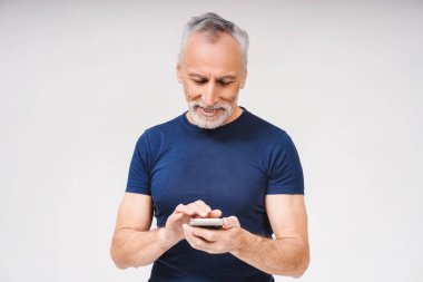 Akıllı telefon tutan, mesaj yazan, stüdyoda poz veren, beyaz tenli, olgun sakallı, beyaz saçlı bir adamın portresi. İş, çevrimiçi teknoloji kavramı