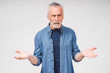 Şok olmuş, yaşlı, gri sakallı bir adamın portresi. Günlük kıyafetler giymiş, el pençe divan duran, kameraya bakan beyaz adam.