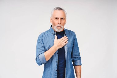 Beyaz arka planda poz veren, elini göğsüne koyup kameraya bakan beyaz saçlı, şaşırmış bir adamın portresi. Halk yaşam tarzı konsepti