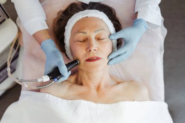 Olgun bir kadının yüz hidro mikro dermabrüksiyon tedavisi gördüğü kozmetik güzellik kaplıca kliniğinde yakın çekim. Yenilenme, kozmetoloji kavramı