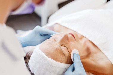 Yaşlı, olgun bir kadın, kaplıcada yatan hasta, estetik ameliyatlar. Kozmetik uzmanı yüz derisini nemlendiriyor, kaldırıyor. Cilt bakımı kavramı, kozmetoloji kavramı