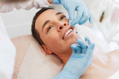 Yakından, genç, çekici bir adam kozmetik ameliyatlar yaptırıyor kozmetik uzmanı elinde şırınga tutuyor modern kozmetik kliniğinde dudak büyütme ameliyatı yapıyor. Cilt bakımı kavramı, kozmetoloji