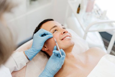 Kozmetik kliniğinde yatan çekici genç adam, kırışıklıkları yok etmek için göz kenarına botoks yapıyor. Kozmetik prosedürleri, kozmetik bilimi kavramı