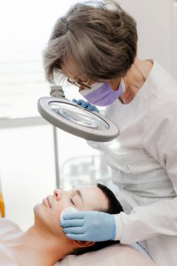 Profesyonel kozmetik uzmanı, modern kozmetik kliniğinde hasta genç ve çekici bir adamın yüz derisini temizliyor. Kozmetik kavramı, sivilce tedavisi, cilt bakımı